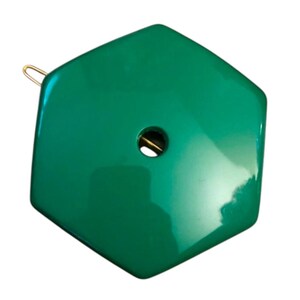 Pode incluir: Uma presilha de cabelo hexagonal verde-esmeralda brilhante com uma superfície lisa e reflexiva. O acessório apresenta um recorte circular central e um mecanismo de mola de metal dourado fino visível no lado esquerdo para prender o cabelo.