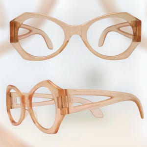 May include: Two pairs of vintage-style spectacles. The frames are a light peach colour with a geometric shape. The lenses are clear. One pair is viewed from the front, and the other is from the side.