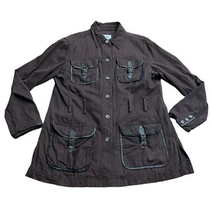 May include: A brown cotton jacket with multiple pockets and leather accents. The jacket has a button-up front and long sleeves.
