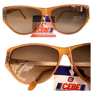 Könnte beinhalten: Eine Sonnenbrille mit braunem Kunststoffgestell und einem CEBE-Etikett. Die Sonnenbrille hat ein umschließendes Design und braune Gläser.
