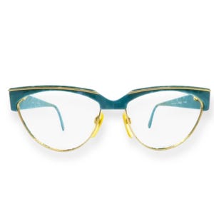 Könnte beinhalten: Türkise Cat-Eye-Brille mit goldfarbenem Rahmen. Die Gläser sind klar.