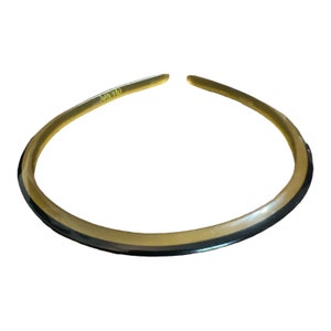 May include: A circular, open-ended neck ring featuring a two-tone design with a translucent amber-colored top section and a solid black bottom section. The piece has a smooth, polished finish and a continuous, curved shape that forms a wide collar.