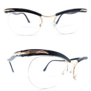 Op de afbeelding: Een paar zwarte cat-eye brillen met gouden accenten en heldere glazen. De bril wordt in twee aanzichten getoond, een met de bril recht en de andere met de bril gekanteld om het zijprofiel te tonen.