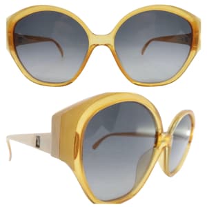 May include: A pair of amber-colored plastic sunglasses with large, round lenses and a gradient gray tint. The sunglasses have a thick frame and a retro style.