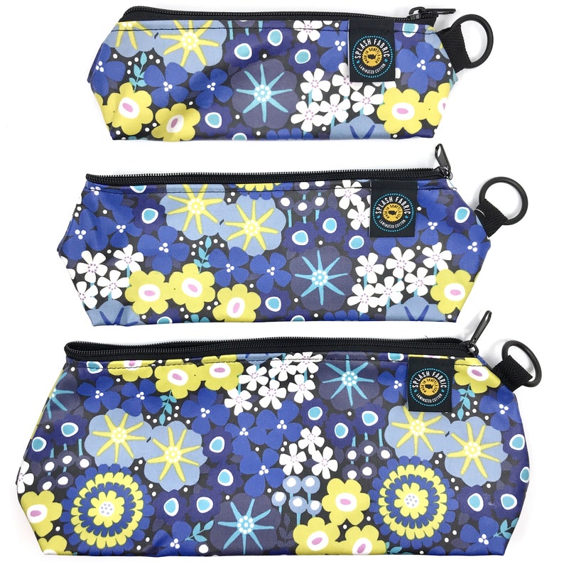 May include: Three zippered pouches with a floral print in shades of blue, yellow, white, and black. The pouches have a black zipper and a black strap with a metal ring.