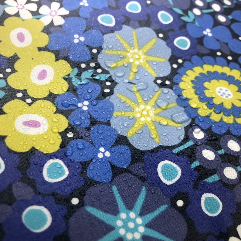 May include: A close-up of a fabric with a repeating pattern of blue, yellow, and white flowers. The fabric is covered in water droplets.