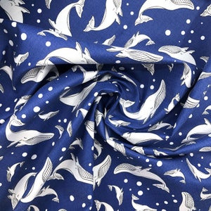 May include: Blue fabric with a white whale pattern. The whales are of different sizes and are swimming in different directions. There are also white dots scattered throughout the fabric.