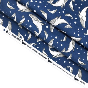 May include: Blue fabric with a white whale pattern and white polka dots. The fabric has the text "SPLASH FABRIC", "FOOD-SAFE", "ECO-FRIENDLY", "THIS FABRIC IS MAGIC", and "If your ship doesn't come in, swim out to it!" printed on it.