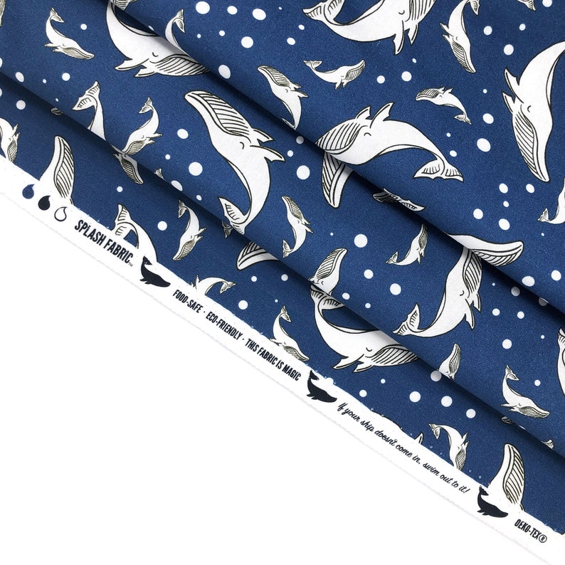 May include: Blue fabric with a white whale pattern and white polka dots. The fabric has the text "SPLASH FABRIC", "FOOD-SAFE", "ECO-FRIENDLY", "THIS FABRIC IS MAGIC", and "If your ship doesn't come in, swim out to it!" printed on it.