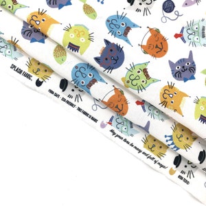 May include: White fabric with a repeating pattern of colorful cartoon cats. The cats have various expressions and wear accessories like glasses and bow ties. The fabric also features text that reads "SPLASH FABRIC" and "FOOD-SAFE - ECO-FRIENDLY - THIS FABRIC IS MAGIC."