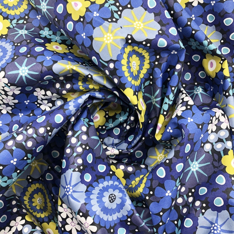 May include: Blue fabric with a repeating pattern of yellow and blue flowers. The fabric is folded and the pattern is visible on both sides.