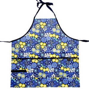 May include: A blue and yellow floral print apron with black trim and two pockets. The apron has adjustable neck straps.