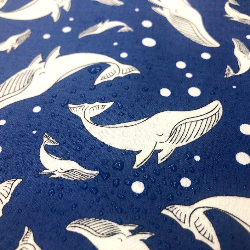 May include: A blue fabric with a white whale pattern. The whales are swimming in a sea of white dots. The fabric has a subtle water droplet texture.