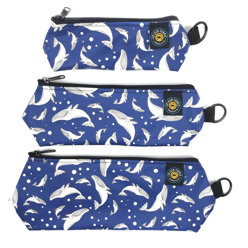 May include: Three blue zippered pouches with a white whale pattern and white polka dots. The pouches have black zippers and black handles. The pouches are labeled "Splash Fabric".