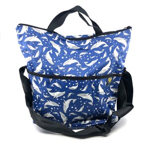 May include: A blue tote bag with a white whale pattern and white polka dots. The bag has a black zipper and a black shoulder strap.