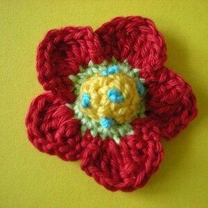 May include: A crocheted flower with red petals and a yellow center with blue accents.