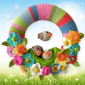 May include: A colourful crocheted wreath featuring a variety of flowers and birds. The wreath is made with a range of colours, including pink, green, blue, and yellow. The flowers are crocheted in various shapes and sizes. The birds are crocheted in a simple design and are perched on the wreath.