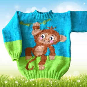 Puede incluir: Un suéter de punto azul y verde con un diseño de mono marrón. El mono se está agarrando a una rama y tiene una expresión feliz.