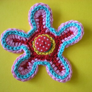 May include: A crocheted flower with pink, red, and blue yarn, featuring a red button with white polka dots in the center.