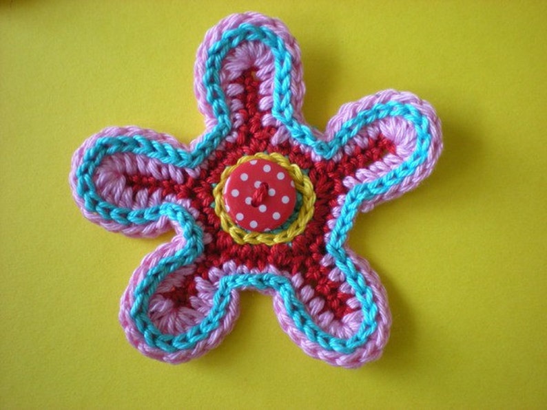 May include: A crocheted flower with pink, red, and blue yarn, featuring a red button with white polka dots in the center.