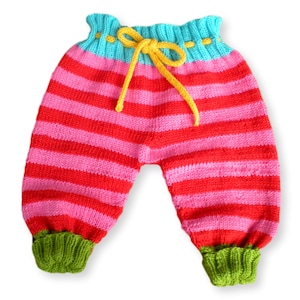 May include: Striped knitted baby pants with a yellow drawstring and green cuffs. The pants are red and pink with horizontal stripes.