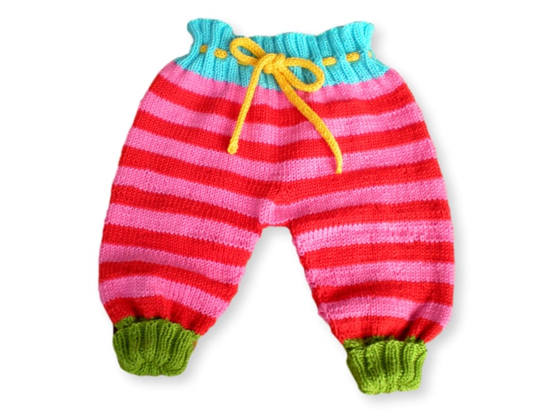 May include: Striped knitted baby pants with a yellow drawstring and green cuffs. The pants are red and pink with horizontal stripes.