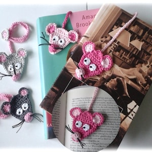 May include: Four crocheted mouse bookmarks in pink and gray with black whiskers. The bookmarks are attached to books with pink yarn.