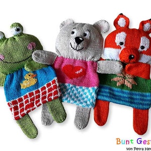 May include: Three handmade knitted animal toys: a green frog, a gray bear, and a red fox. The frog wears a blue shirt with a yellow duck, the bear a pink shirt with a red heart, and the fox a green and blue skirt.