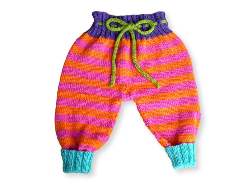 May include: Striped knitted baby pants with a purple waistband and green drawstring. The pants have orange and pink stripes and turquoise cuffs.