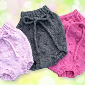 May include: Three pairs of knitted baby bloomers in pink, gray, and light pink with a textured bobble pattern. Each pair has a bow tie at the waist.