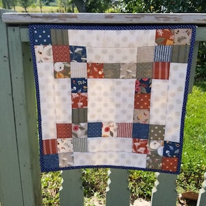 May include: A patchwork quilt with a white background and squares of various colors and patterns, including red, blue, green, and brown. The quilt is edged with a navy blue trim with white polka dots.