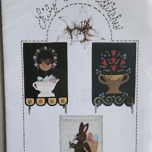 May include: Three felt spring banners with a bird in a nest, a vase of tulips, and a bunny holding a flower. The banners are labeled "Spring Banners" and "Pattern LAS910".