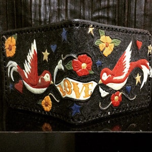 May include: Black leather wallet with a colorful tattoo-style design. The design includes two red birds, flowers, stars, hearts, and the word "LOVE" on a banner. The wallet is rectangular and has a stitched border.