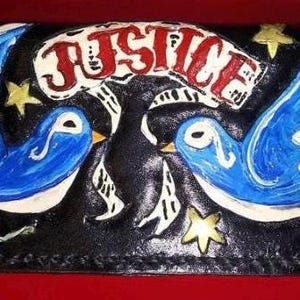 May include: Black leather wallet featuring two blue birds with white accents, yellow stars, and a red rose. The word "JUSTICE" is written in red and white across the top. A unique, hand-painted design.