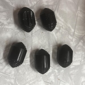 May include: Five black, oval-shaped buttons with a ridged, spiral design. The buttons have a slightly tapered shape and a smooth, matte finish. The buttons are likely for clothing or craft projects.