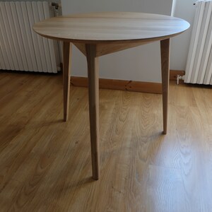 Puede incluir: Una mesa redonda de madera con un acabado de madera clara y tres patas. La mesa est&aacute; sobre un suelo de madera dura.