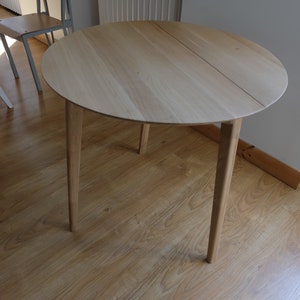 Puede incluir: Una mesa redonda de madera con un acabado en madera clara y cuatro patas. La mesa est&aacute; hecha de madera maciza y tiene un dise&ntilde;o simple y moderno.