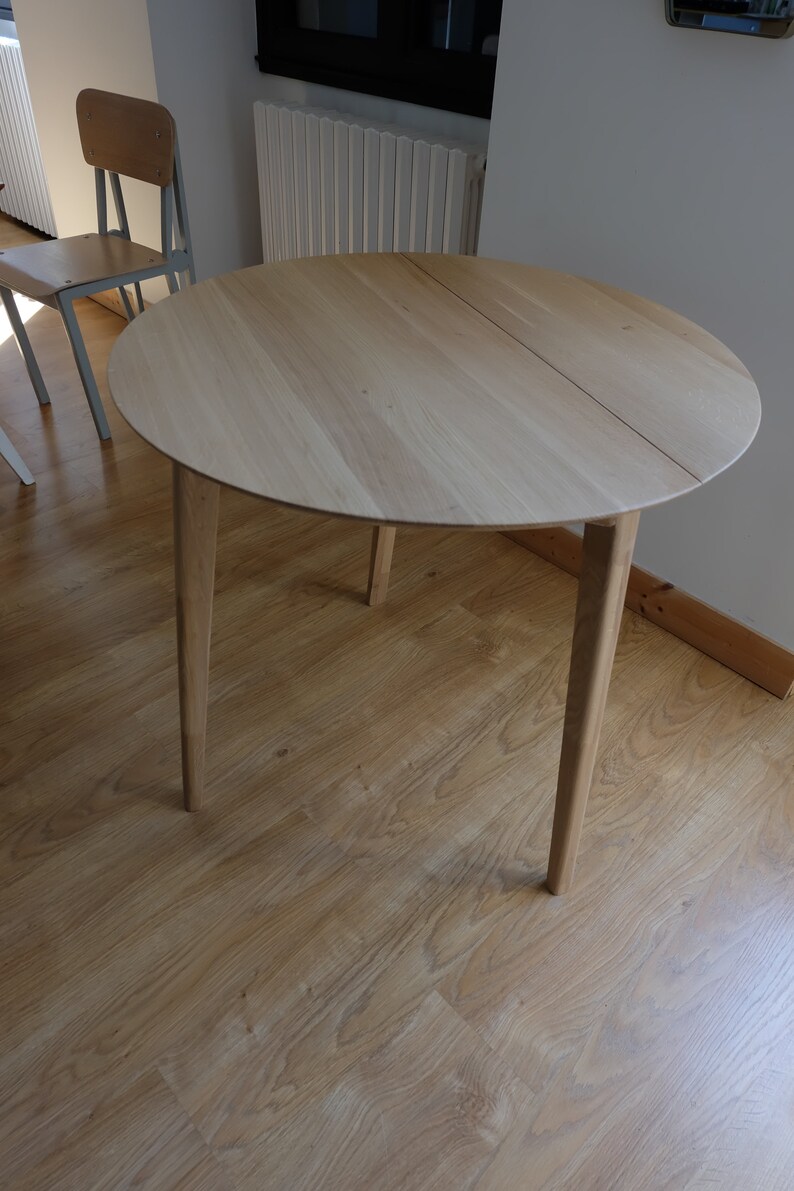 Puede incluir: Una mesa redonda de madera con un acabado en madera clara y cuatro patas. La mesa est&aacute; hecha de madera maciza y tiene un dise&ntilde;o simple y moderno.