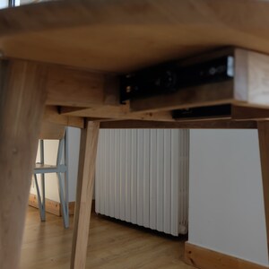 Puede incluir: Una mesa de madera con un caj&oacute;n oculto que se desliza sobre rieles met&aacute;licos. La mesa tiene un acabado marr&oacute;n claro y est&aacute; sostenida por cuatro patas.
