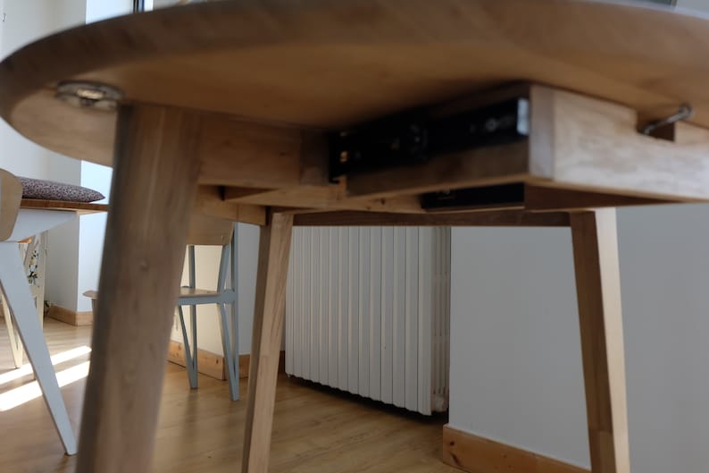 Puede incluir: Una mesa de madera con un caj&oacute;n oculto que se desliza sobre rieles met&aacute;licos. La mesa tiene un acabado marr&oacute;n claro y est&aacute; sostenida por cuatro patas.