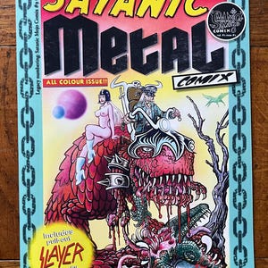 May include: A comic book cover featuring a large, red, scaly monster with a toothy mouth. The monster is riding a motorcycle with a woman in a black and white outfit sitting on the back. The title of the comic is "Satanic Metal Comix".