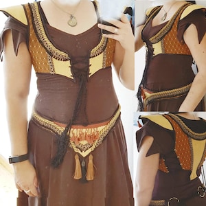 May include: A brown and gold corset with a lace-up front and a brown skirt. The corset has a gold trim and a brown and gold patterned fabric. The skirt has a gold belt with tassels.