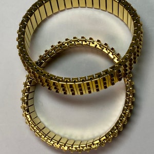 May include: Two gold-toned expandable bracelets with a linked chain design. The bracelets are stacked on top of each other.
