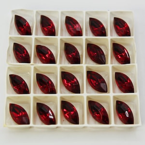 May include: A clear plastic container with 20 red, marquise-shaped rhinestones. The rhinestones are arranged in a grid pattern.