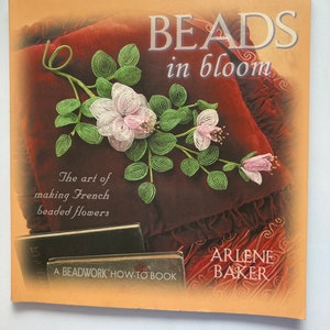 May include: The book cover of "BEADS in bloom" displays a beaded floral design in pink, white, and green. The cover also includes the text "The art of making French beaded flowers" and "A BEADWORK HOW-TO BOOK".
