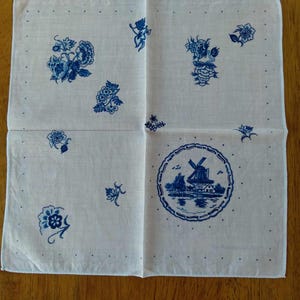 May include: White handkerchief with blue floral and windmill designs. The handkerchief features scattered floral patterns and a central circular design with a windmill scene. Small dots border the edges.