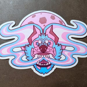 May include: A sticker featuring a stylized wolf with a pink and blue color scheme. The wolf has a fierce expression with bared teeth, set against a pink moon background. Swirling smoke-like elements in pink and blue frame the wolf's head.