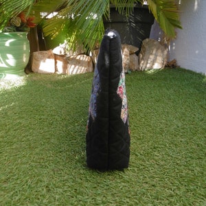 Pu&ograve; includere: Borsa tote trapuntata nera con un colorato motivo floreale sul davanti. La borsa ha una forma rettangolare e una chiusura a cerniera. Lo sfondo &egrave; erba verde.