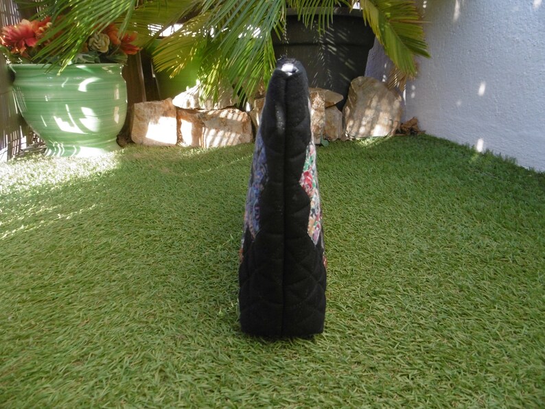 Pu&ograve; includere: Borsa tote trapuntata nera con un colorato motivo floreale sul davanti. La borsa ha una forma rettangolare e una chiusura a cerniera. Lo sfondo &egrave; erba verde.