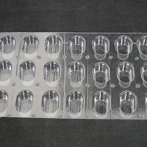 May include: Clear plastic mold with 16 oval-shaped cavities. The mold is rectangular with rounded corners and is designed for creating small, individual treats. The cavities are evenly spaced and have a smooth, glossy finish.